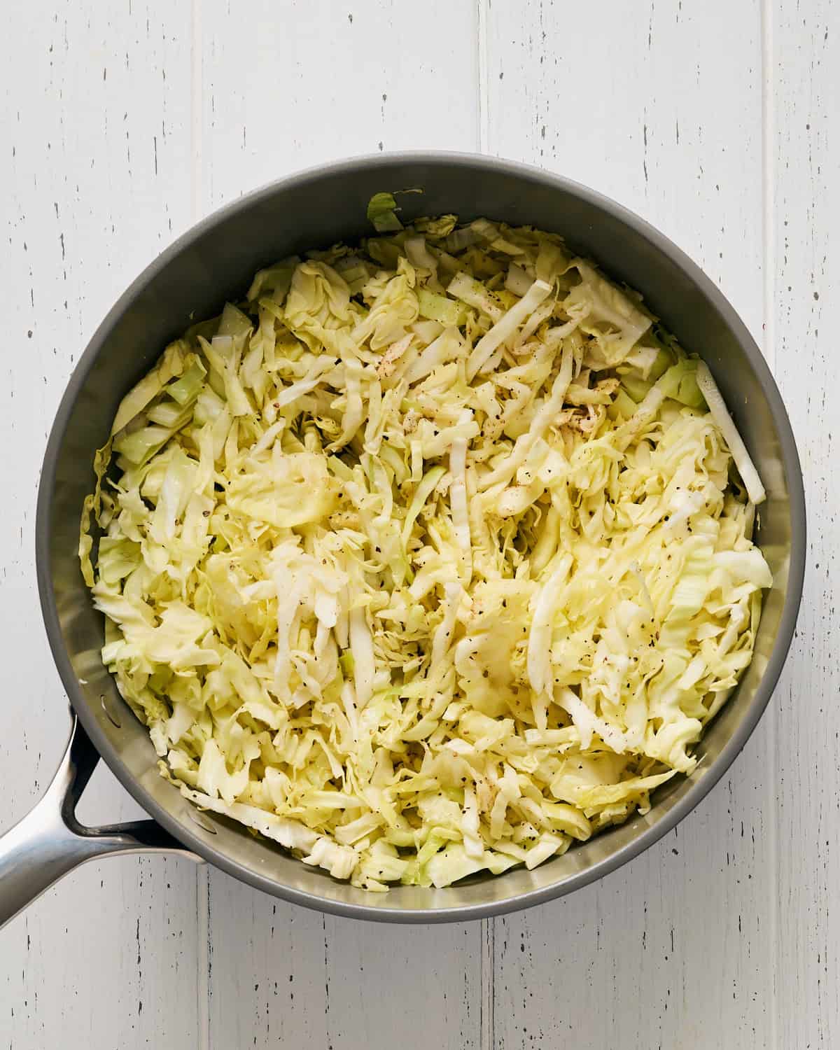 Cooking sliced cabbage and garlic with olive oil and seasoning in a saucepan.