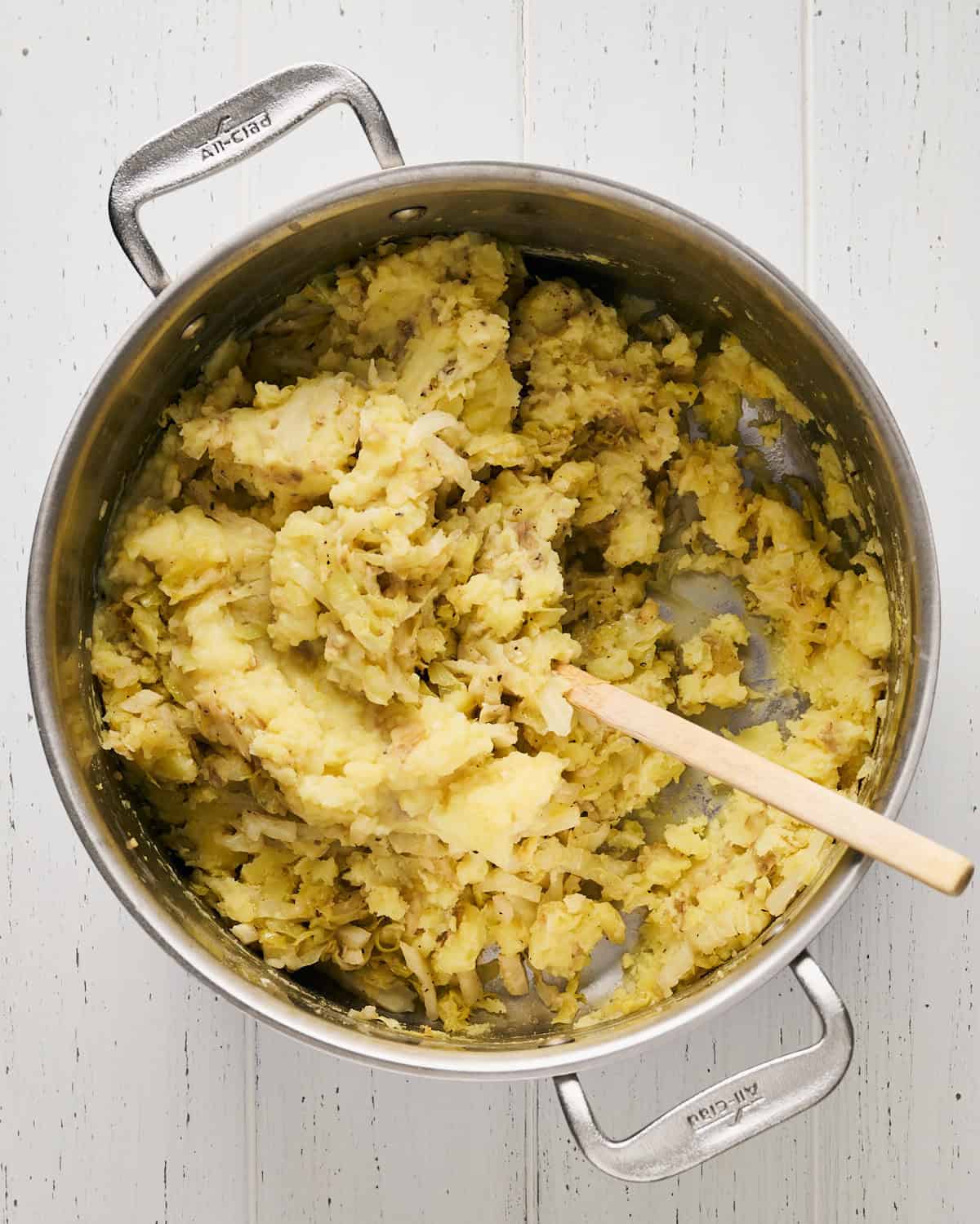 Mixing mashed Yukon gold potatoes with cabbage in a large pot.