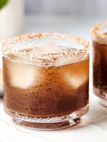 Glass filled with tamarindo margarita rimmed with tajin and salt.