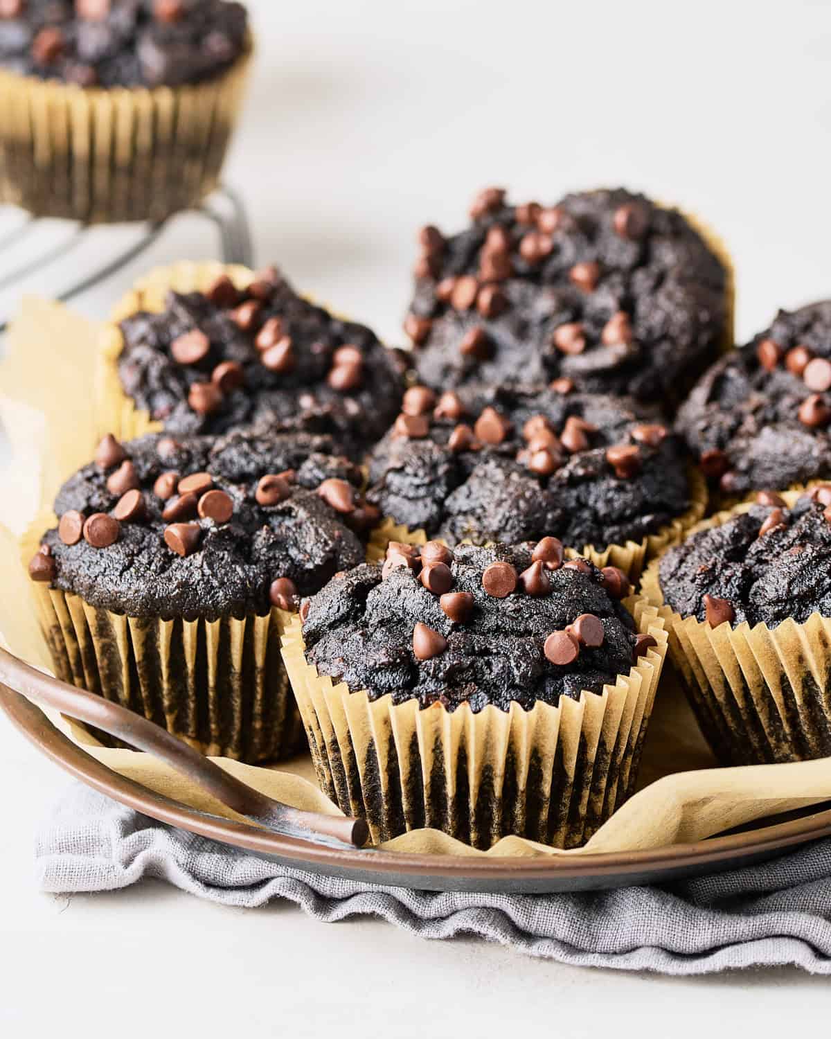 A round tray with seven vegan chocolate sweet potato muffins on parchment paper.